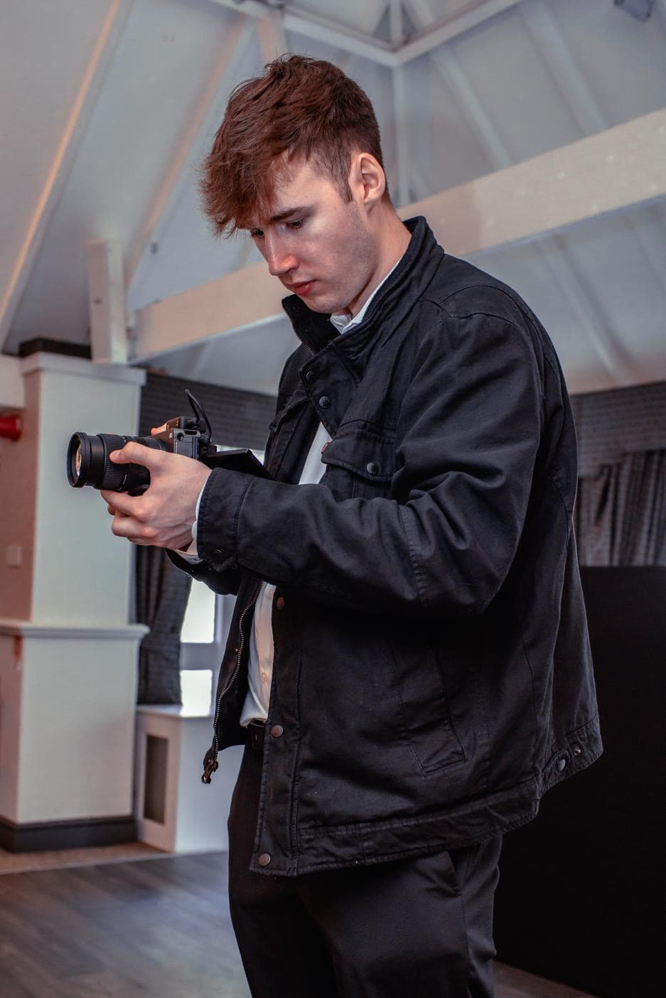 Young man in a black jacket holding a professional camera and looking at the screen.