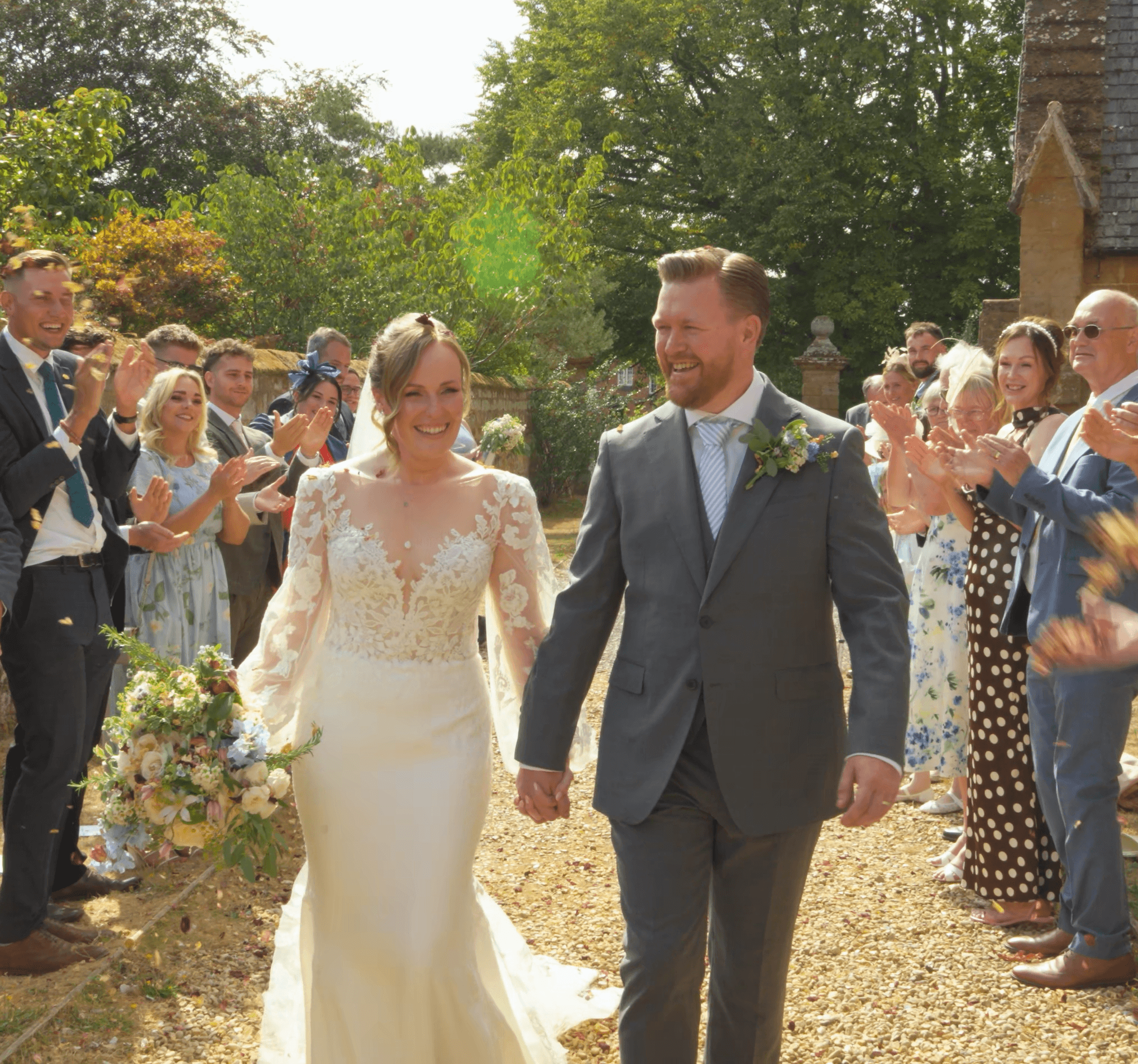 Smiling bride and groom walking through a shower of confetti thrown by cheering wedding guests.